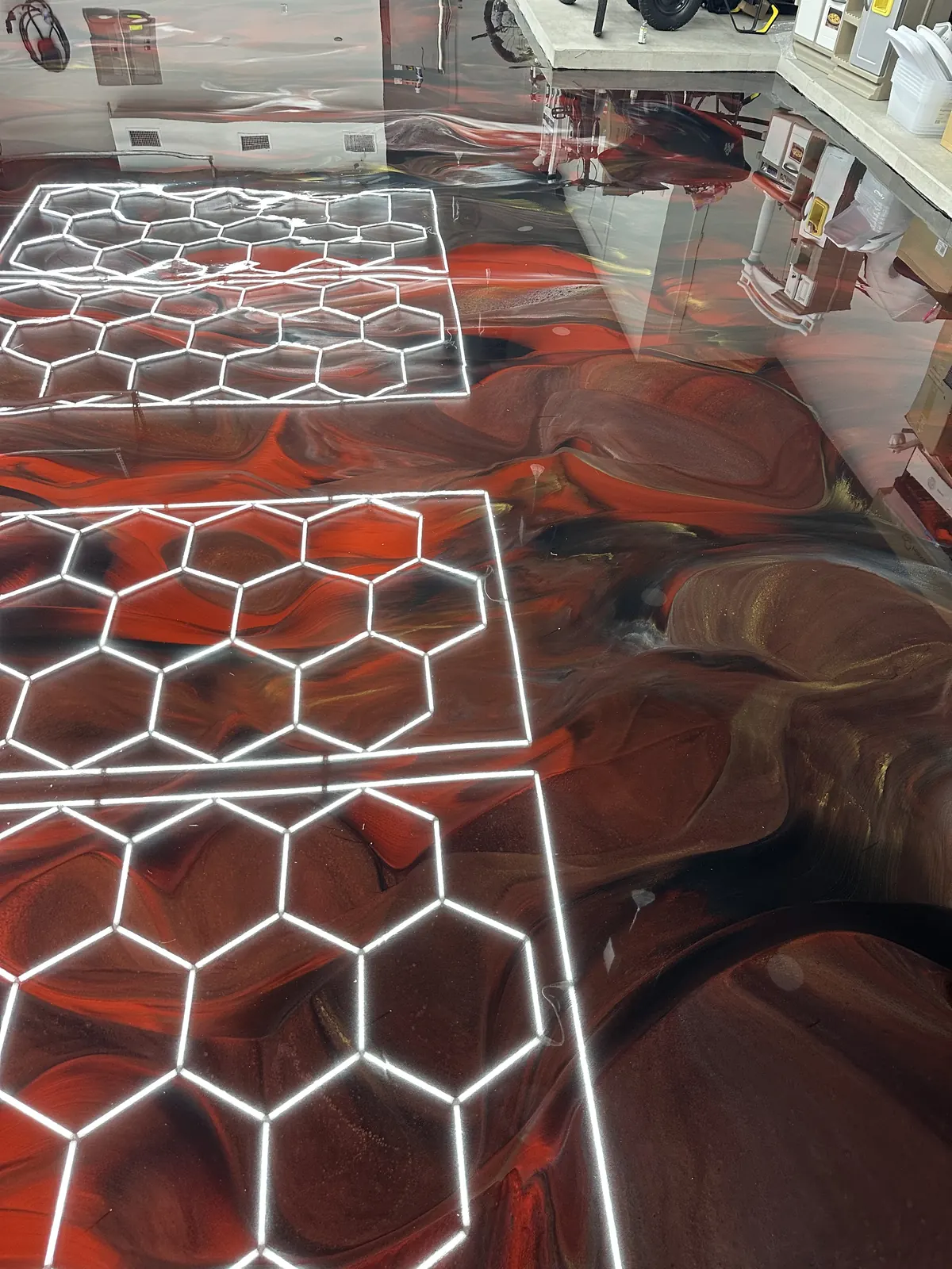 Red metallic epoxy floor under hexagon lights in a detailing studio, view 3